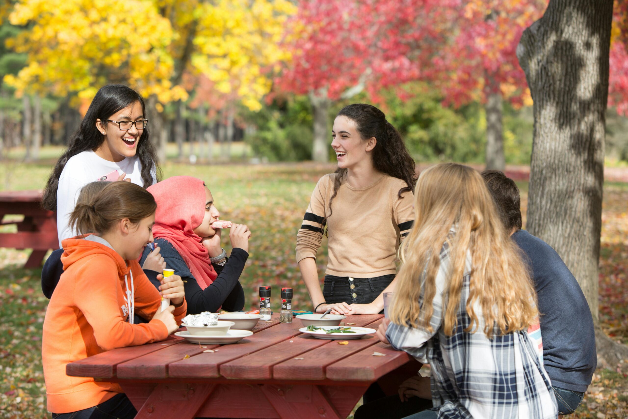 A diverse group of friends laughing and enjoying a picnic at a vibrant park in fall.